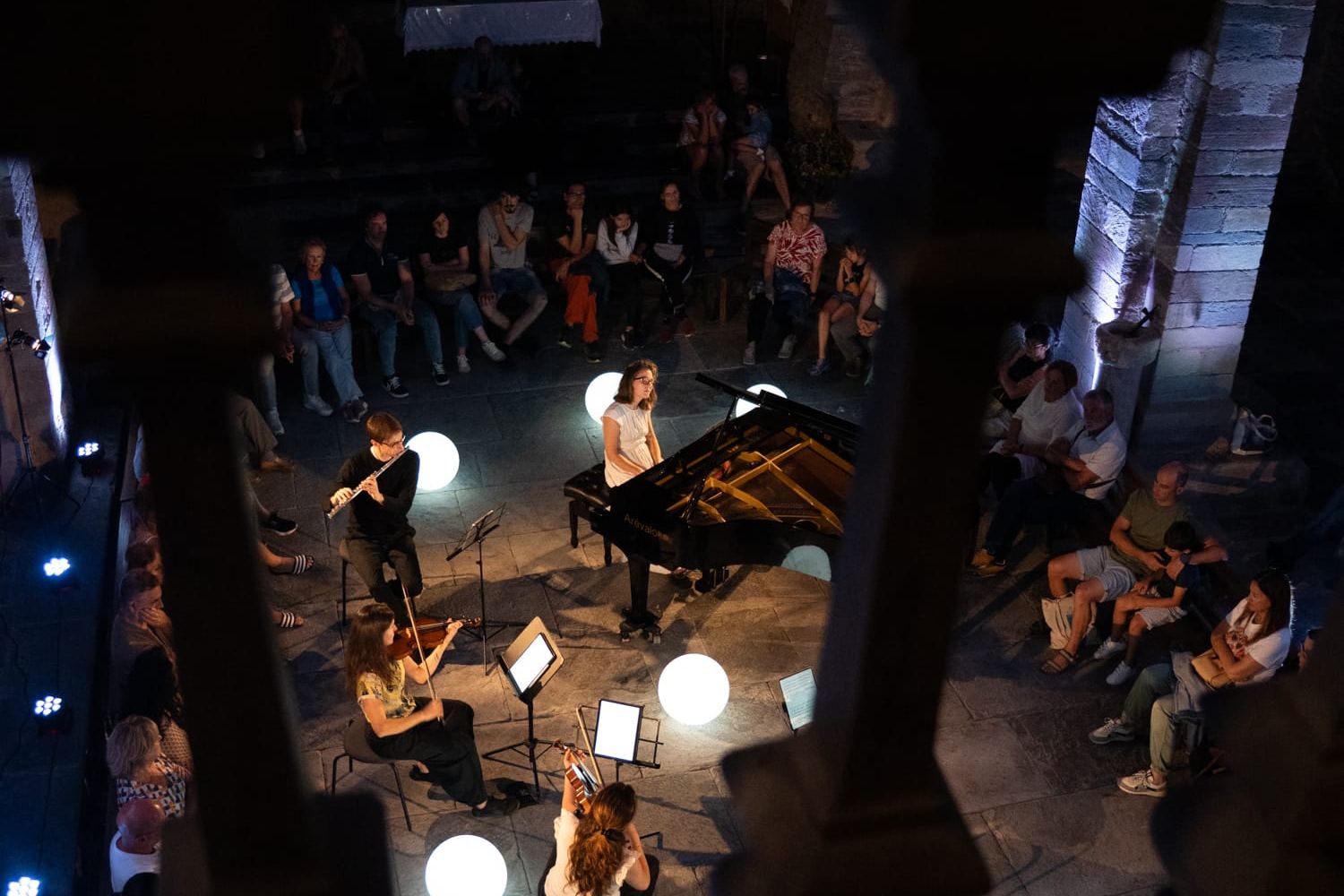 Concierto visto desde arriba en un claustro, con globos de luz alrededor del piano