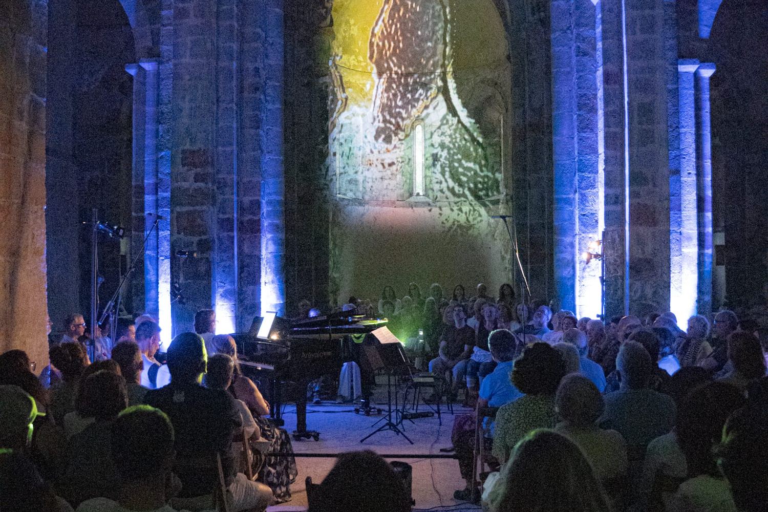 Concierto en una iglesia románica iluminada de azul, con el piano al fondo bajo los arcos