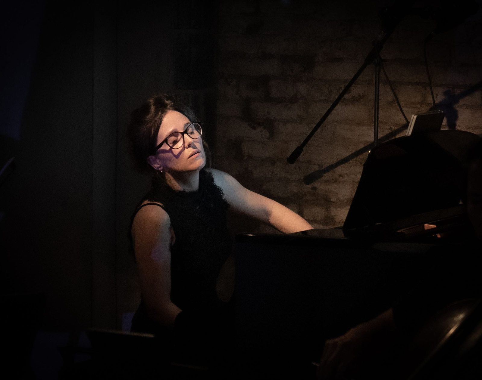 Josefina Urraca al piano, con los ojos cerrados, ante un muro de ladrillo en penumbra