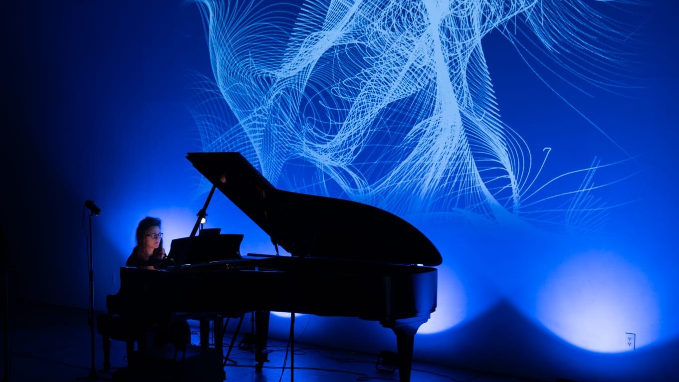 Josefina Urraca al piano en un escenario azul, con una proyección de líneas de luz detrás