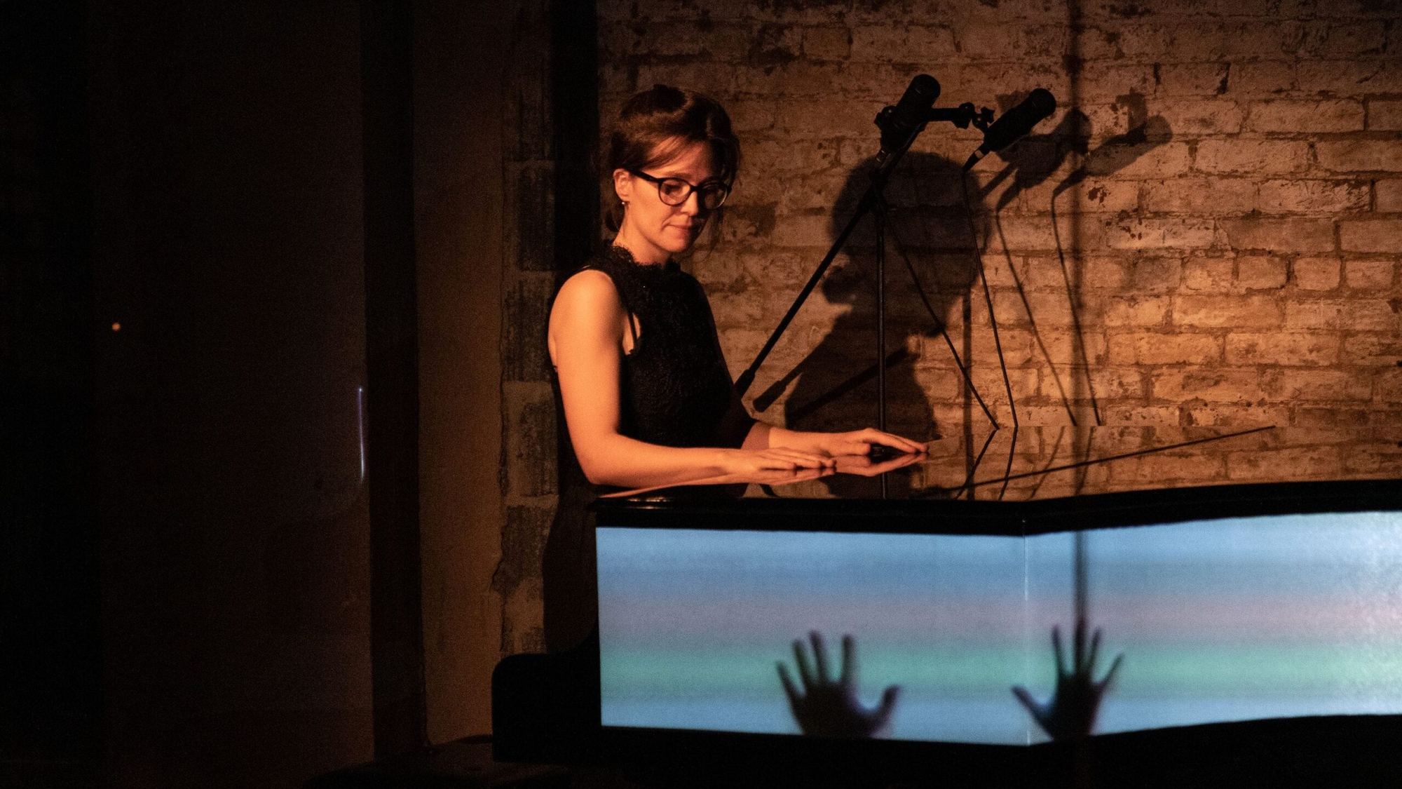 Josefina Urraca al piano ante un muro de ladrillo, con una proyección sobre la tapa del instrumento